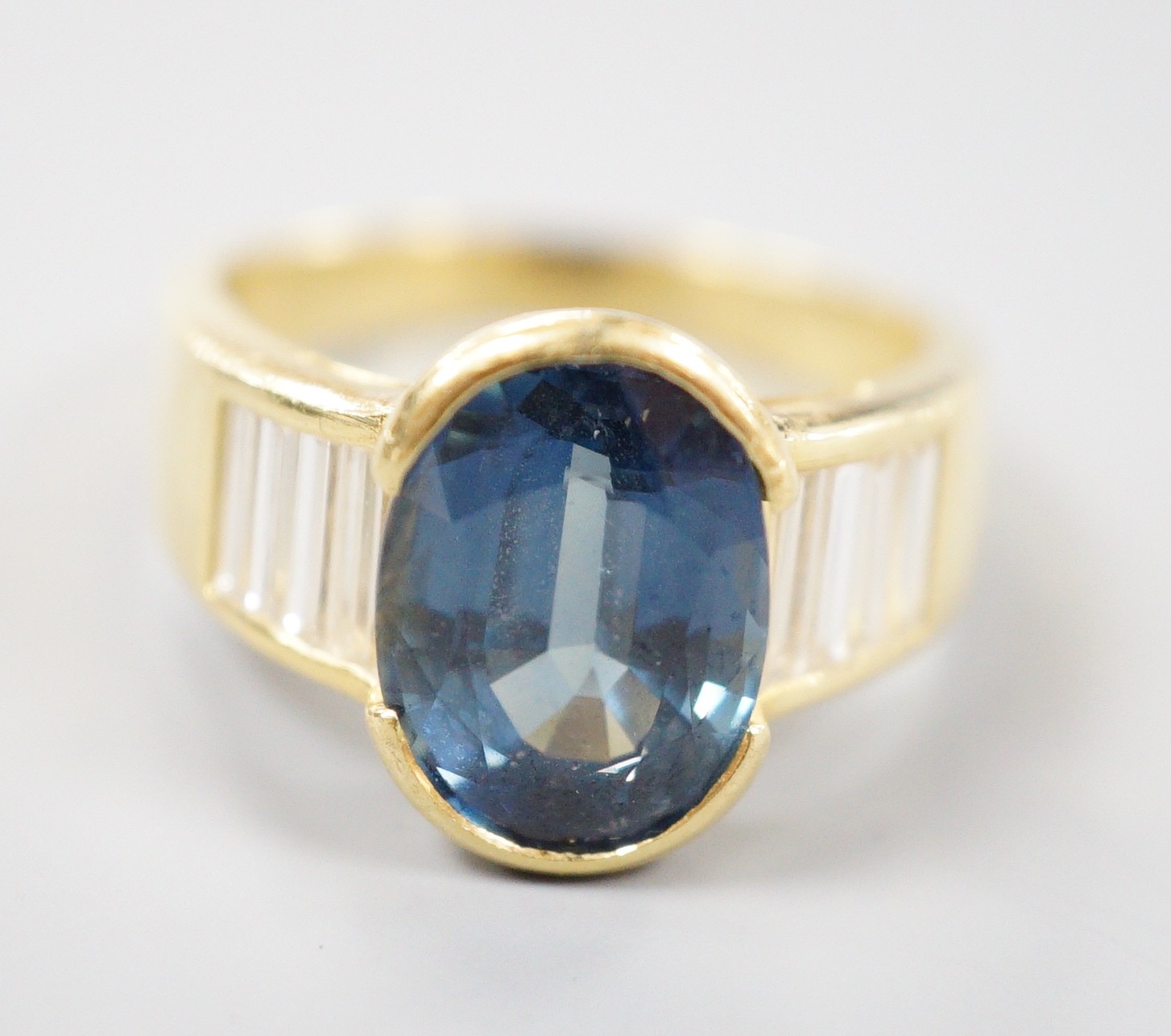 A modern 18ct gold and single stone oval cut sapphire set ring, with baguette cut diamond set shoulders, size R, gross weight 8.3 grams.